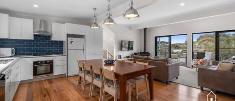 Une cuisine moderne avec un coin repas, un salon doté d’une cheminée et de grandes fenêtres offrant une vue dégagée.