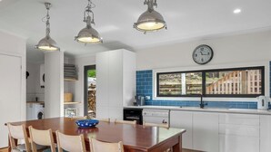 Une cuisine moderne avec des meubles blancs, un plan de travail recouvert de carreaux bleus, un coin repas avec une table et des chaises en bois, et des luminaires suspendus.