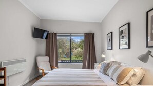 Une chambre à coucher avec un lit, une chaise, un bureau, une télévision et une fenêtre avec des rideaux.