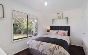 A bedroom with a large window, a bed with a dark headboard, and a bedside table with a lamp. - Between Waters At Yanakie (Yanakie)