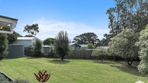 Un jardin avec une pelouse, des arbres, une clôture et un bâtiment doté d’un toit en métal.
