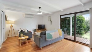 Un salon comprenant un canapé, un téléviseur, une lampe et une porte-fenêtre coulissante donnant sur un jardin.