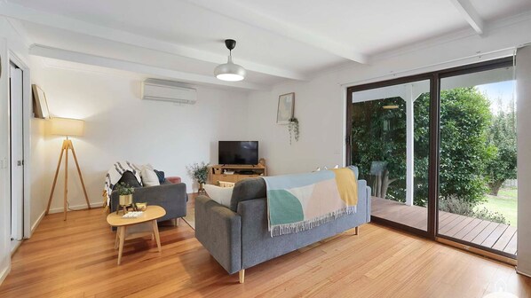 A living room with a sofa, a TV, a lamp, and a sliding glass door leading to a garden.