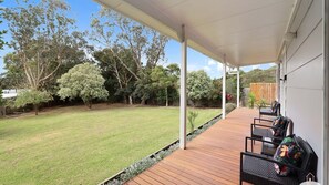 A covered outdoor area with a wooden deck, chairs, and a view of a grassy yard with trees. - Between Waters Stay 3 Pay 2 Winter Special (Yanakie)