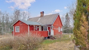 Une maison en bois rouge, avec un toit en pente, une cheminée et un petit porche.
