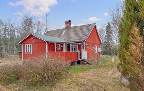 A red wooden house with a sloped roof, a chimney, and a small porch.