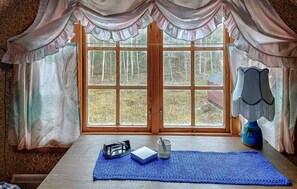 A room with a large window, a wooden table with a blue mat, a metal tray, and a blue vase.