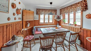 Une cuisine chaleureuse avec des lambris en bois, une table à manger avec des chaises, une fenêtre avec des rideaux et un luminaire suspendu.
