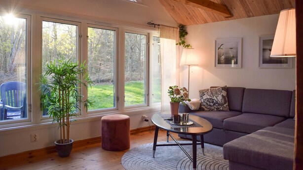 Ein Zimmer mit großem Fenster, einer Couch, einem kleinen Tisch, einer Lampe und einem Blumentopf.