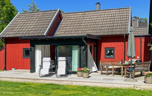 Ein rotes Holzhaus mit Veranda, Sitzgelegenheiten im Freien und Schornstein.
