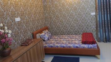 Un dormitorio con una cama, un aparador de madera, un florero con flores y papel tapiz estampado.