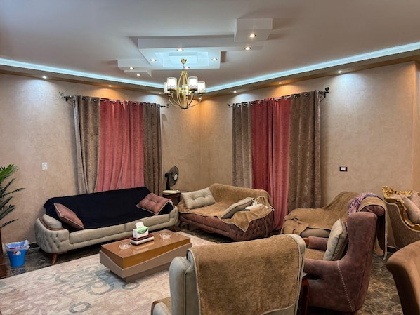 Un salon comprenant un canapé, des fauteuils, une table basse et un lustre.
