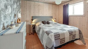 Ett sovrum med en väggpanel av trä, en säng med ett mönstrat täcke, ett sängbord med lampor och ett fönster med gardiner.