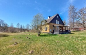 Ein zweistöckiges Haus mit Veranda, umgeben von einem Rasen und Bäumen.