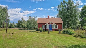 A red house with a blue door, surrounded by a grassy field and trees. - 2 bedroom cozy home in Tingsryd (Tingsryd)