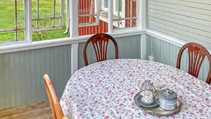 A dining area with a table covered in a floral tablecloth, wooden chairs, and a window with red shutters. - 2 bedroom cozy home in Tingsryd (Tingsryd)