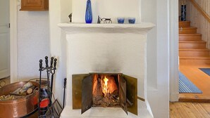 A fireplace with a burning fire, a metal candelabra, and a copper pot filled with logs.