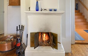 A fireplace with a burning fire, a metal candelabra, and a copper pot filled with logs.