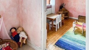 Ein Zimmer mit einem Holztisch, Stühlen, einer kleinen Holzkabine und einem farbenfrohen Teppich.