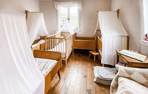 A room with two wooden cribs, a small wooden table, a window with a view, and a white curtain. - 2 bedroom nice home in Glömminge (Glömminge)