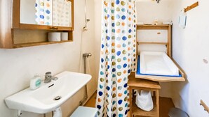 Ein kleines Badezimmer mit einem Waschbecken, einer Duschvorhang mit Punkten, einem Holzregal und einer kleinen Mülleimer.