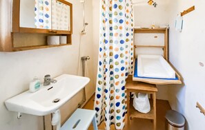 A small bathroom with a sink, a shower curtain with polka dots, a wooden shelf, and a small trash bin. - 2 bedroom nice home in Glömminge (Glömminge)