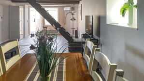 A dining area with a wooden table, chairs, a striped rug, and a plant centerpiece.