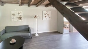 A loft-style room with a gray sofa, a small round table with a candle, and two floral paintings on the walls.