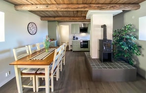 Un comedor con mesa y sillas de madera, una cocina con estufa y un reloj en la pared.
