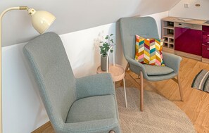 A room with a grey armchair, a matching sofa, a small side table with a plant, a colorful pillow, and a wooden floor. - 3 bedroom beautiful home in Klintehamn (Klintehamn)