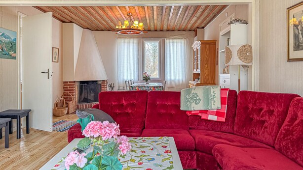 A cozy living room with a red sofa, a fireplace, and a dining area with a table and chairs. - 2 bedroom amazing home in Visby (Visby)