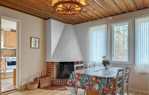 A dining area with a fireplace, a table with a colorful tablecloth, wicker baskets, and a view of the outside through large windows. - 2 bedroom amazing home in Visby (Visby)