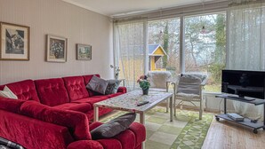 A living room with a red sofa, a small table, a TV, and a view of a house through large windows. - 2 bedroom amazing home in Visby (Visby)