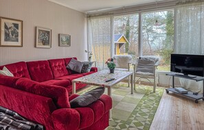A living room with a red sofa, a small table, a TV, and a view of a house through large windows. - 2 bedroom amazing home in Visby (Visby)