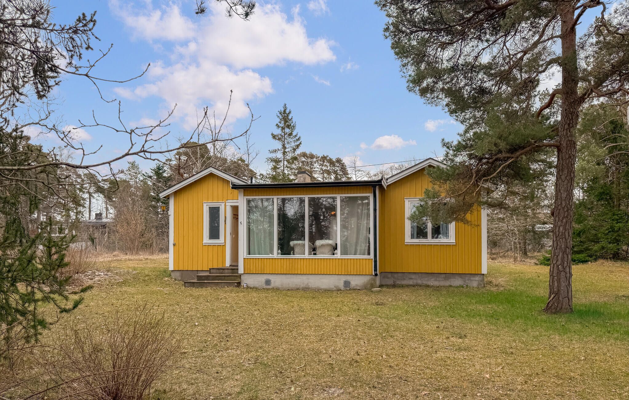 A yellow cabin with a large window, a door, and a small porch.
