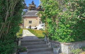 Ein Wohngebäude mit Backsteinfassade, einer sichtbaren Treppe zum Eingang und einem Gartenbereich mit Stufen und Blumentöpfen.