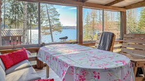 A cozy cabin with a large window overlooking a lake, a wooden table with a floral tablecloth, and a bench. - Awesome home in Grythyttan with lake view (Grythyttan)