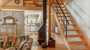 A loft-style room with a wooden staircase, a sofa, a fireplace, and a kitchen in the background. - Awesome home in Grythyttan with lake view (Grythyttan)