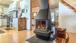 A modern kitchen with a wood-burning stove, wooden cabinets, and a dining area with a view of the outdoors. - Awesome home in Grythyttan with lake view (Grythyttan)