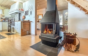 A modern kitchen with a wood-burning stove, wooden cabinets, and a dining area with a view of the outdoors.