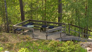 A wooden deck with seating and a table, surrounded by a forest. - Gorgeous home in Värmdö (Värmdö)