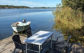 A wooden dock with a table and chairs, a small boat, and a calm lake with a forested island in the background. - Lovely home in Värmdö (Värmdö)
