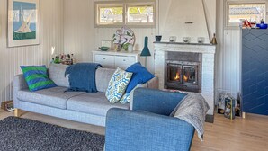 A cozy living room with a fireplace, a sofa, and a window overlooking a garden. - Gorgeous home in Värmdö (Värmdö)