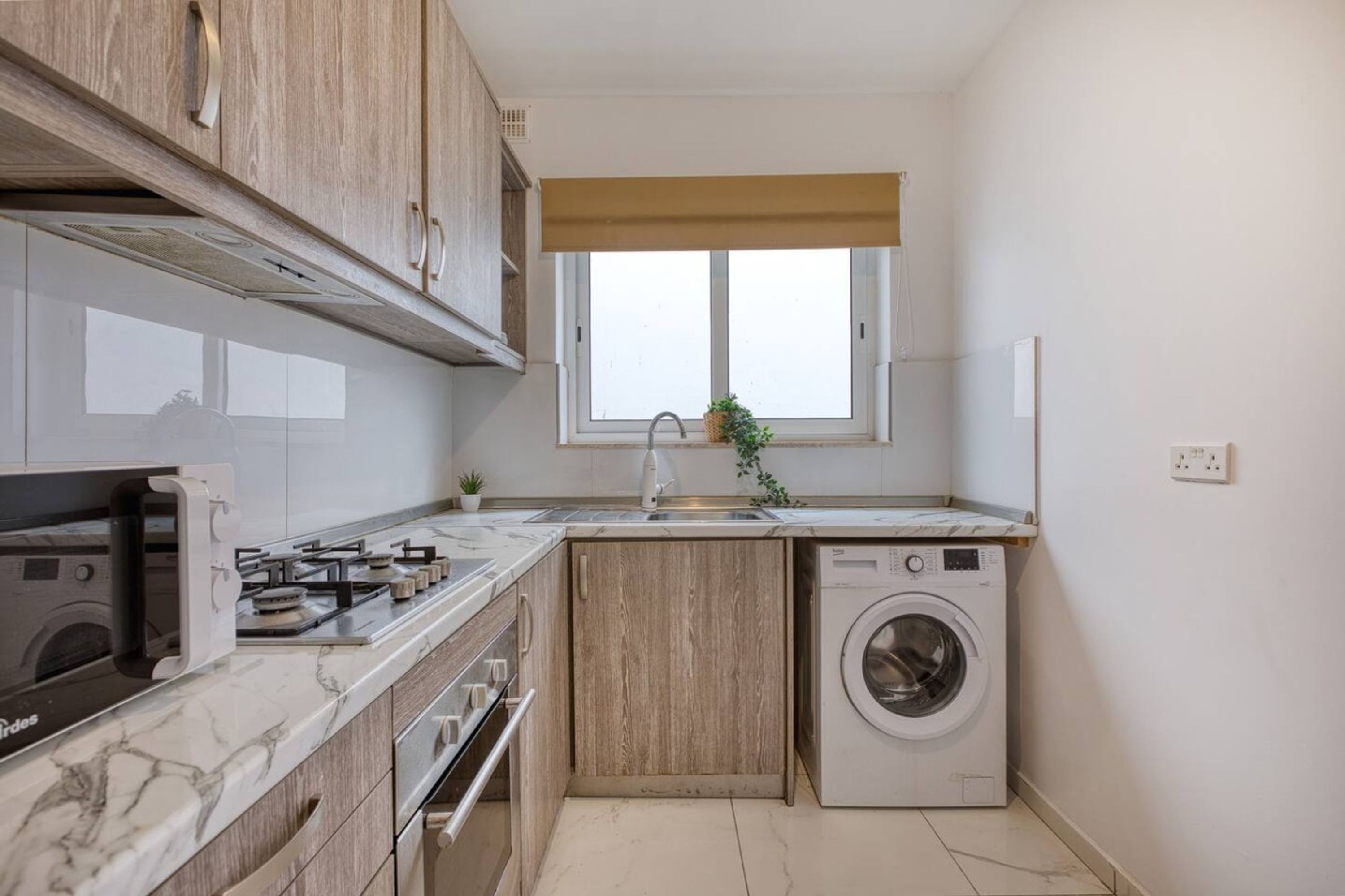 Uma cozinha compacta com forno embutido, micro-ondas, máquina de lavar e janela com vista.