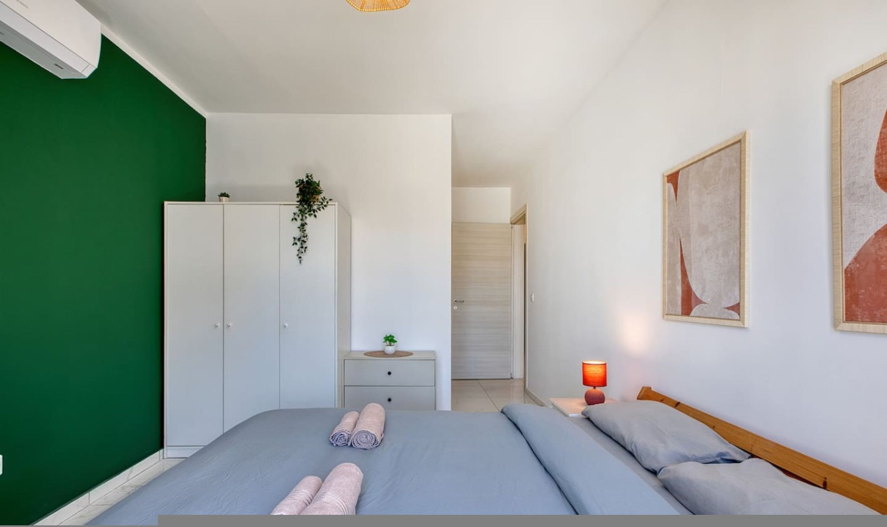 A bedroom with a bed, a wardrobe, a bedside table, a lamp, and a painting.