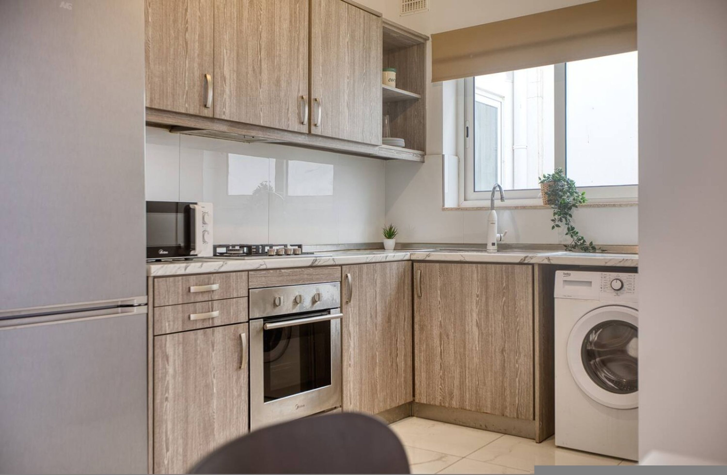 A modern kitchen with wooden cabinets, a built-in oven, a microwave, and a washing machine.