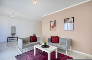Una sala de estar moderna con dos sofás grises, una mesa de centro blanca, un tapete rojo y dos cuadros enmarcados en la pared.