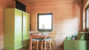 Interior de una cabaña de madera con una mesa de comedor, sillas, un sofá verde y una ventana.
