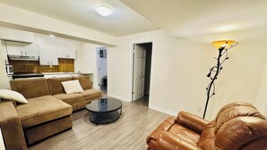 A living room with a sofa, a coffee table, and a leather armchair. There is a kitchen in the background with cabinets and a stove. - Spacious, Private & Independent Stay in Milton (Milton)