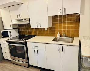 A kitchen with white cabinets, a microwave, a stove, and a sink.